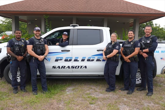 Members of the Sarasota Police Department’s Homeless Outreach Team stand with an SPD vehicle....