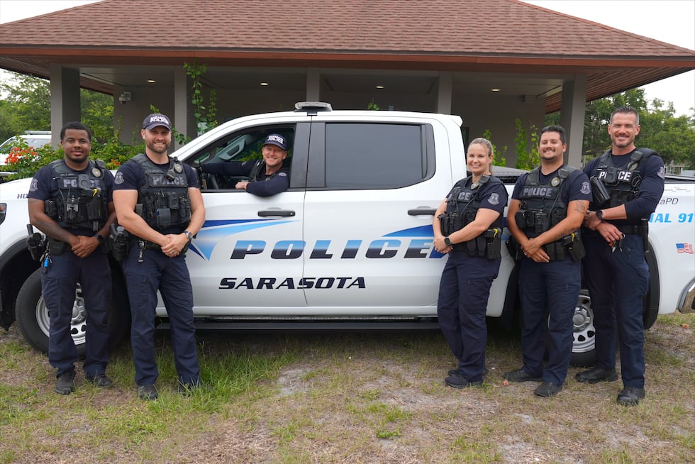 Members of the Sarasota Police Department’s Homeless Outreach Team stand with an SPD vehicle....